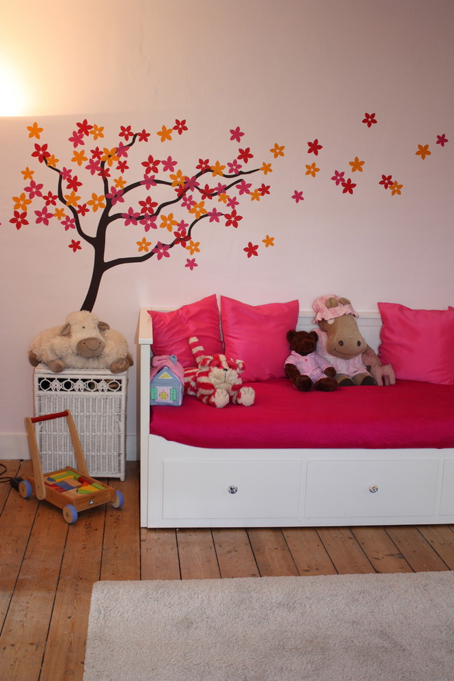 Mid-sized modern kids' room in London with pink walls and medium hardwood floors for girls.