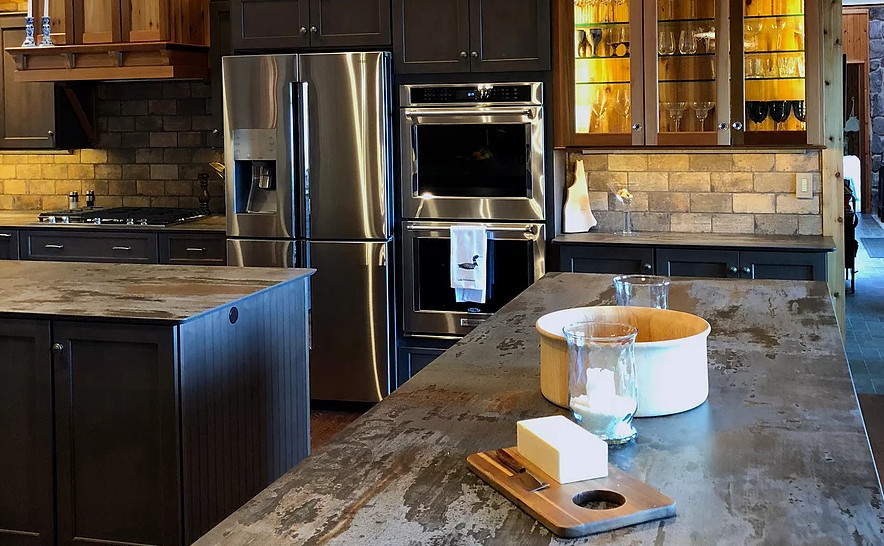 Eat-in kitchen - large rustic u-shaped dark wood floor and brown floor eat-in kitchen idea in Boston with an undermount sink, recessed-panel cabinets, gray cabinets, soapstone countertops, beige backsplash, travertine backsplash, stainless steel appliances, two islands and black countertops