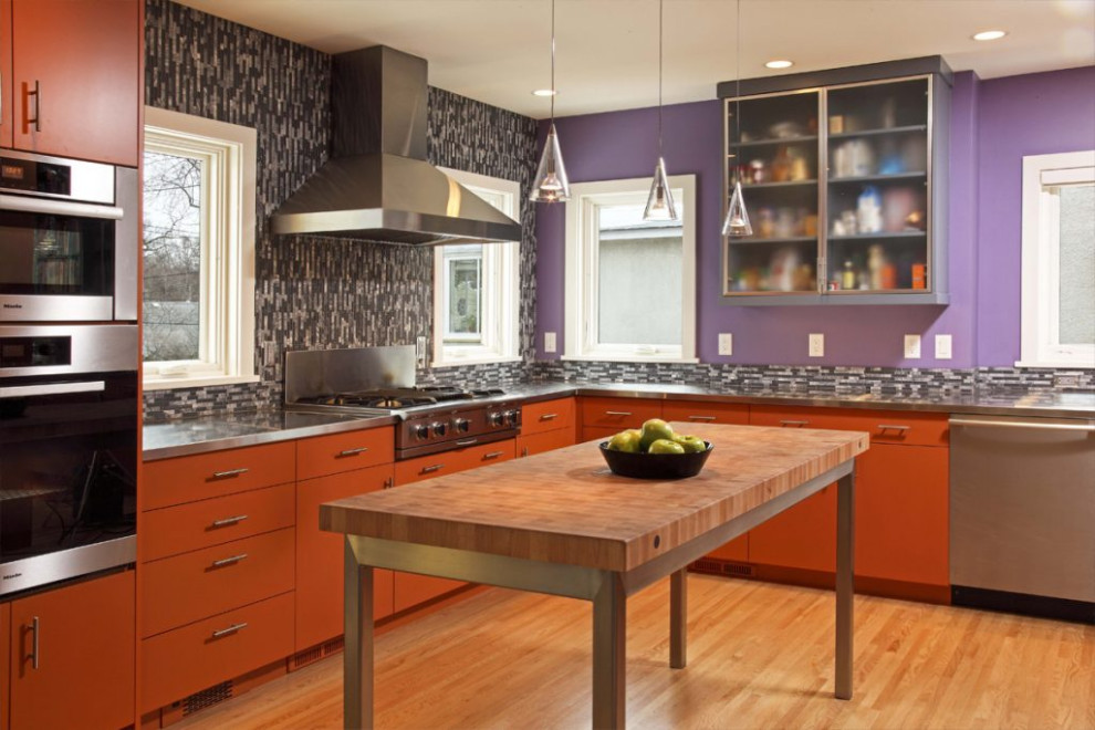 Inspiration for a mid-sized modern l-shaped kitchen in Minneapolis with glass-front cabinets, red cabinets, stainless steel benchtops, multi-coloured splashback, porcelain splashback, stainless steel appliances, light hardwood floors and with island.