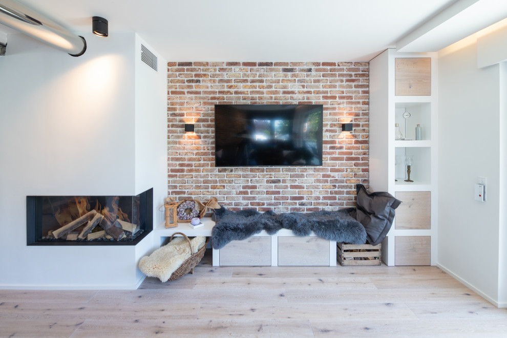 Mid-sized industrial open concept living room in Other with beige walls, medium hardwood floors, a corner fireplace, a plaster fireplace surround, a wall-mounted tv, beige floor and brick walls.