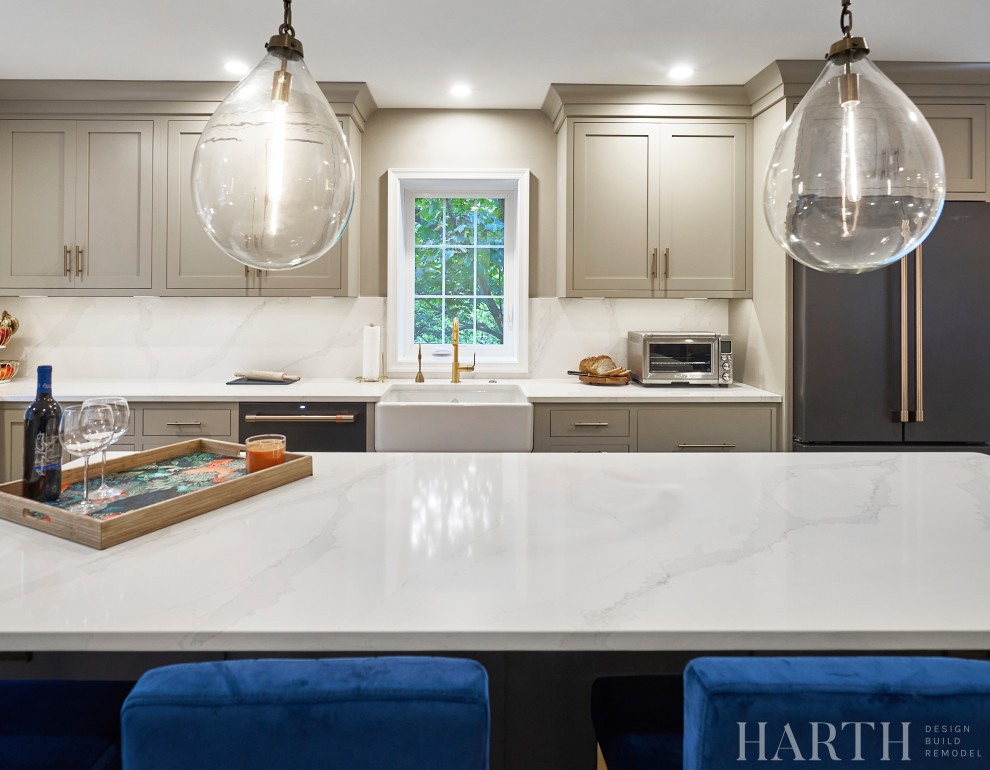 Example of a mid-sized transitional l-shaped porcelain tile and brown floor eat-in kitchen design in Philadelphia with a farmhouse sink, shaker cabinets, beige cabinets, quartz countertops, white backsplash, quartz backsplash, black appliances, an island and white countertops