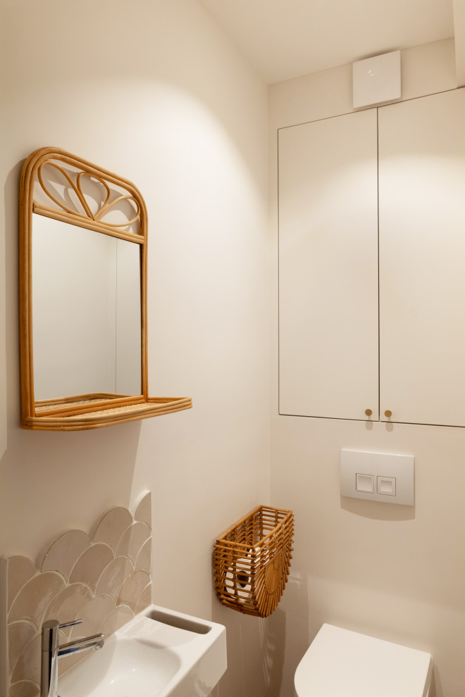 Foto på ett litet lantligt toalett, med luckor med profilerade fronter, beige skåp, en vägghängd toalettstol, beige kakel, mosaik, beige väggar, cementgolv, ett väggmonterat handfat och flerfärgat golv