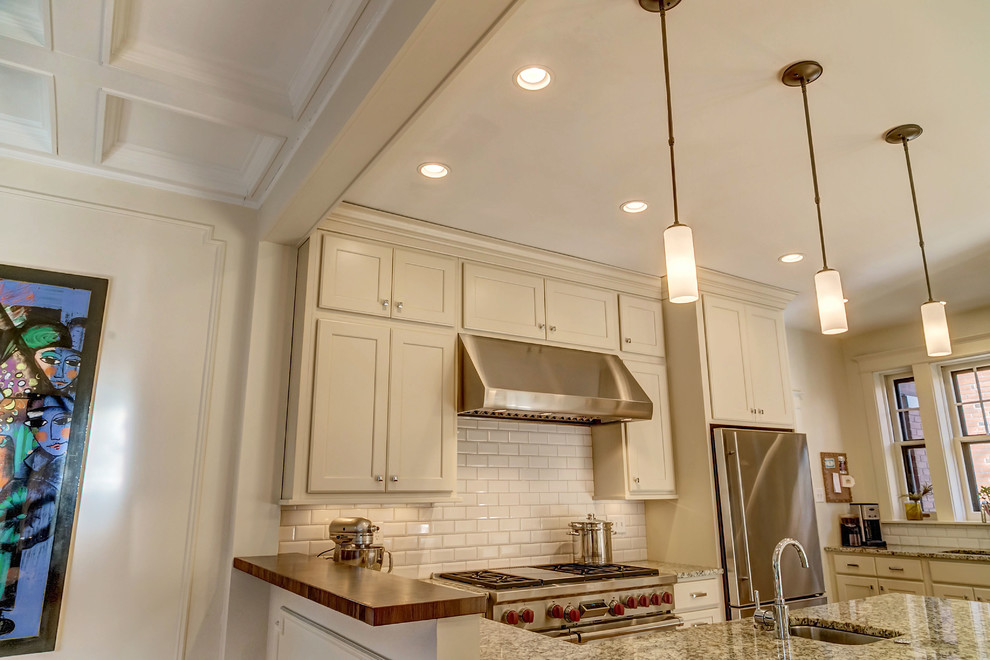 Transitional kitchen photo with an undermount sink, flat-panel cabinets, white cabinets, white backsplash, ceramic backsplash, stainless steel appliances, white walls and a peninsula