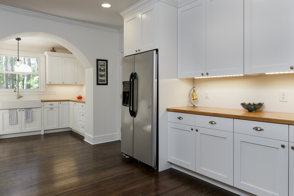 Design ideas for a large transitional l-shaped eat-in kitchen in Raleigh with shaker cabinets, white cabinets, stainless steel appliances, dark hardwood floors, a farmhouse sink, beige splashback, subway tile splashback and no island.