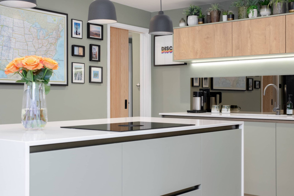 На фото: угловая кухня-гостиная среднего размера в современном стиле с накладной мойкой, плоскими фасадами, серыми фасадами, столешницей из кварцита, зеркальным фартуком, черной техникой, островом и белой столешницей