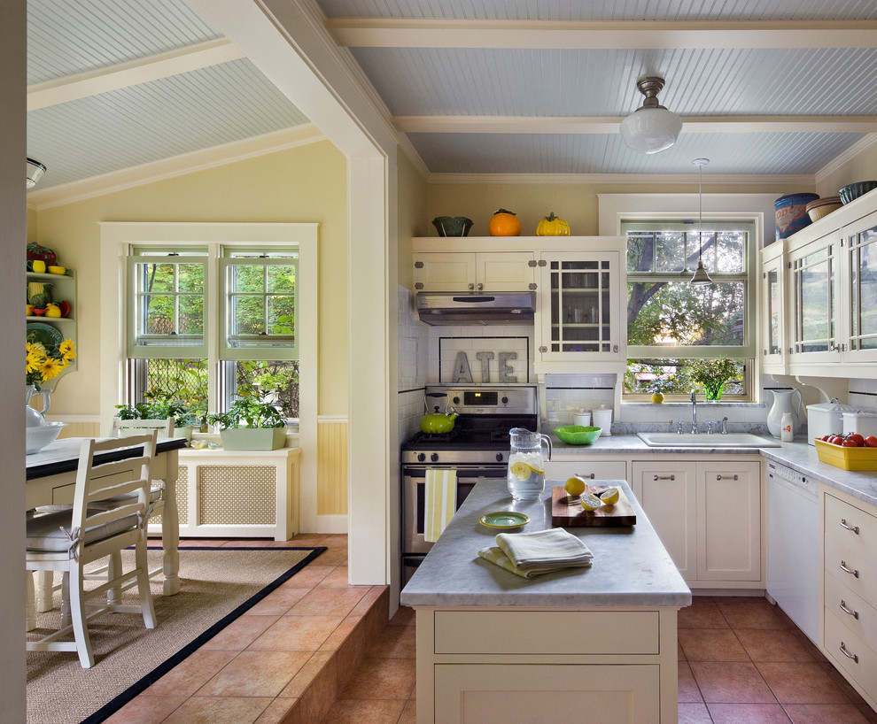 Photo of a traditional eat-in kitchen in New York with a drop-in sink, glass-front cabinets, white cabinets, white splashback, subway tile splashback and stainless steel appliances.