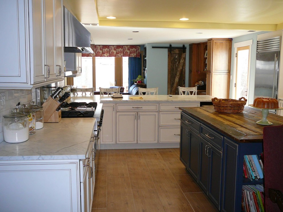 This is an example of a large country galley eat-in kitchen in New York with a farmhouse sink, recessed-panel cabinets, distressed cabinets, marble benchtops, white splashback, ceramic splashback, stainless steel appliances, light hardwood floors and with island.