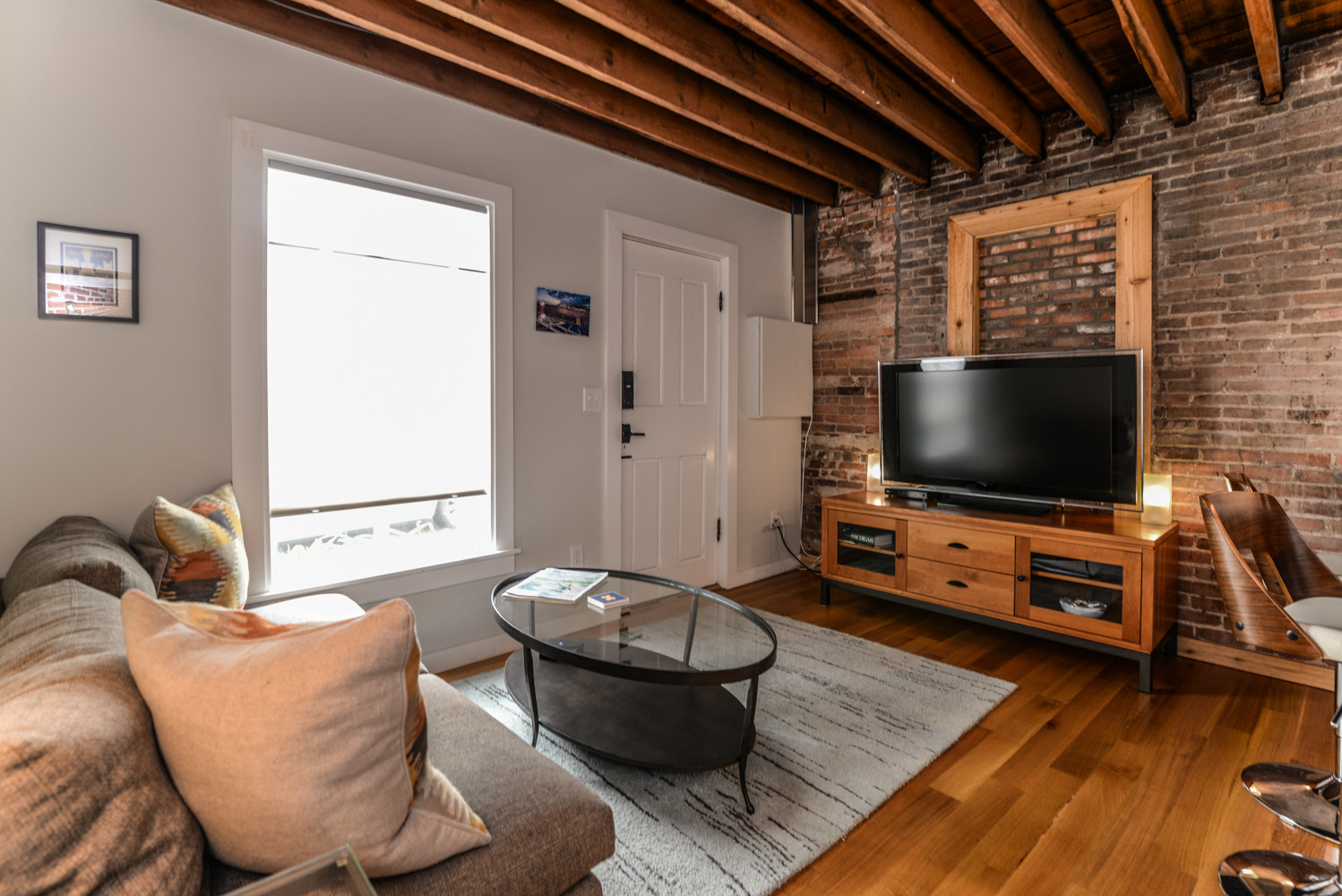 The exposed wood beams and brick give instant warmth to the carriage house loft. Reclaimed wood floors with a natural clear coat finish provide just enough color to the neutral palette of furniture an