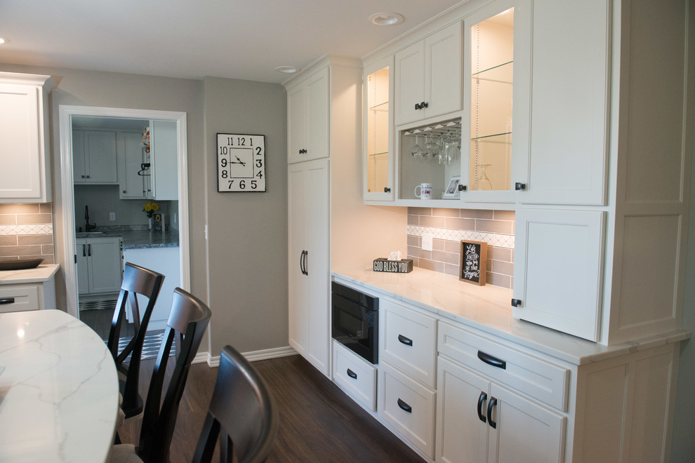 Large transitional u-shaped laminate floor and brown floor eat-in kitchen photo with a double-bowl sink, shaker cabinets, white cabinets, quartz countertops, gray backsplash, subway tile backsplash, stainless steel appliances, an island and white countertops