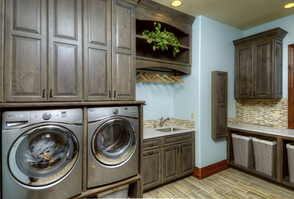 This is an example of a large transitional u-shaped dedicated laundry room in Denver with raised-panel cabinets, blue walls, a side-by-side washer and dryer and dark wood cabinets.