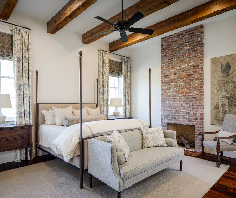 Photo of a large traditional master bedroom in New Orleans with white walls, medium hardwood floors, a standard fireplace, a brick fireplace surround, red floor and exposed beam.