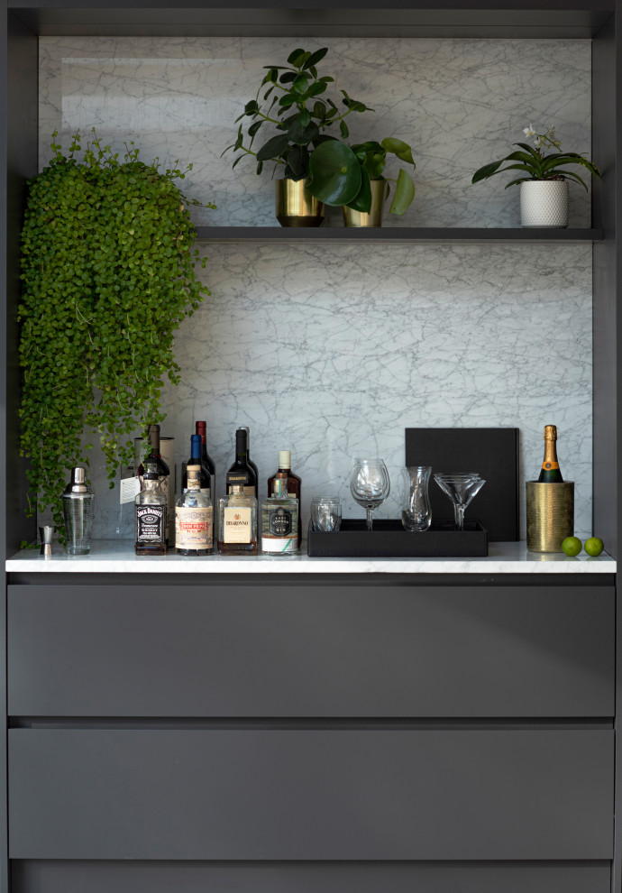 This is an example of a large contemporary home bar in London with grey cabinets, marble benchtops and light hardwood floors.