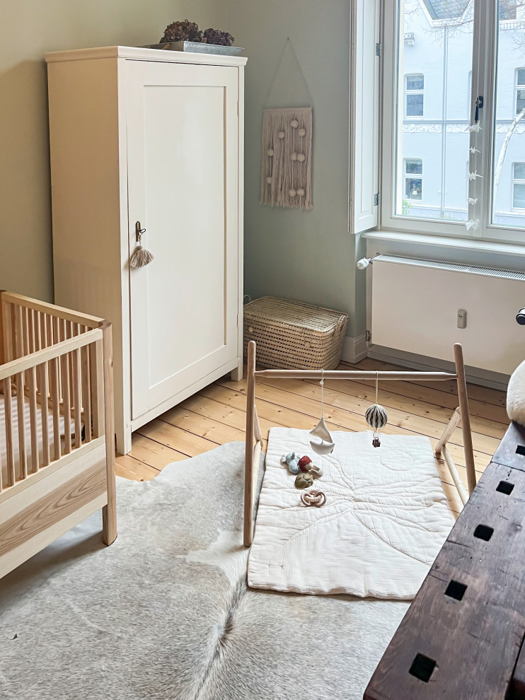 Diseño de habitación de bebé neutra campestre pequeña con paredes verdes, suelo de madera clara y suelo beige