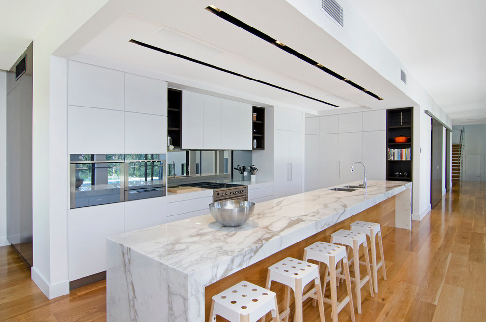 Contemporary l-shaped kitchen in Gold Coast - Tweed with flat-panel cabinets, white cabinets, metallic splashback, mirror splashback and medium hardwood floors.