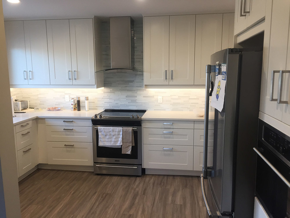 Enclosed kitchen - mid-sized transitional u-shaped medium tone wood floor and brown floor enclosed kitchen idea in Calgary with recessed-panel cabinets, beige cabinets, quartz countertops, white backsplash, stainless steel appliances, a peninsula, white countertops and porcelain backsplash