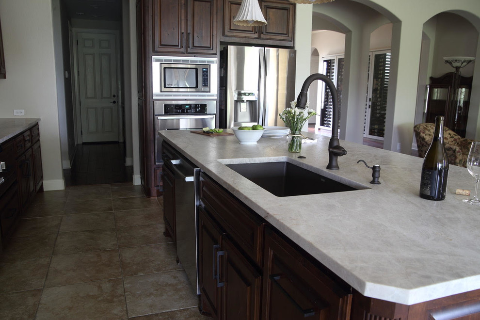 Large transitional l-shaped ceramic tile and beige floor enclosed kitchen photo with an undermount sink, dark wood cabinets, beige backsplash, stainless steel appliances and an island