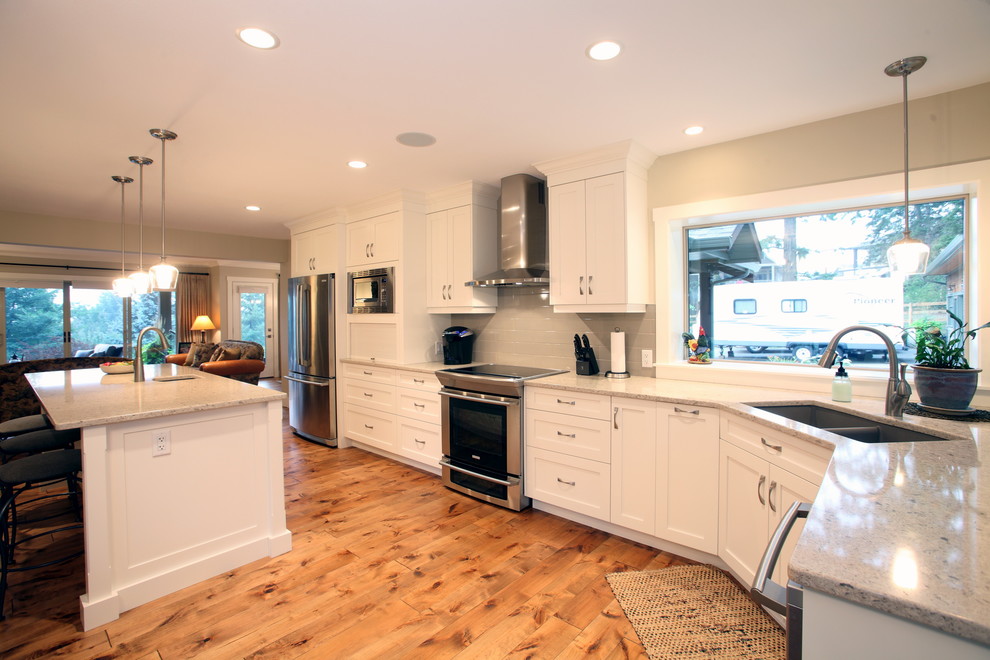 Mid-sized arts and crafts u-shaped kitchen in Vancouver with an undermount sink, shaker cabinets, white cabinets, granite benchtops, white splashback, ceramic splashback, stainless steel appliances, medium hardwood floors and with island.