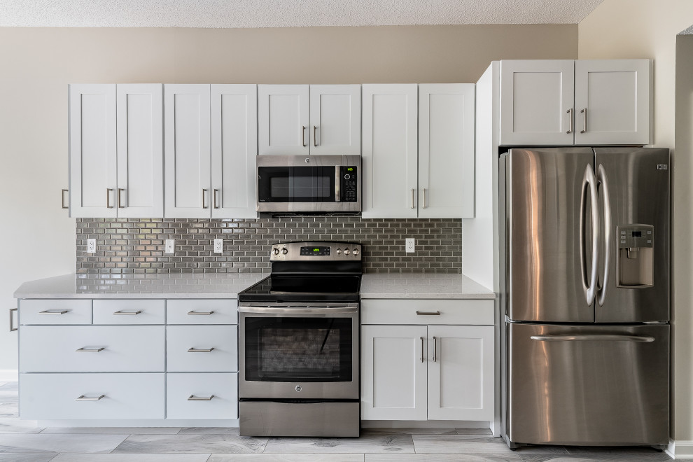 Example of a mid-sized transitional galley porcelain tile and multicolored floor eat-in kitchen design with an undermount sink, recessed-panel cabinets, white cabinets, quartz countertops, gray backsplash, ceramic backsplash, stainless steel appliances, a peninsula and white countertops