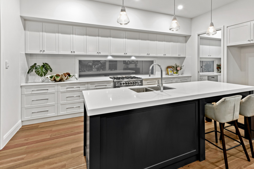 Design ideas for a large contemporary galley kitchen pantry in Brisbane with an undermount sink, shaker cabinets, white cabinets, quartz benchtops, white splashback, subway tile splashback, stainless steel appliances, light hardwood floors, with island, brown floor and white benchtop.