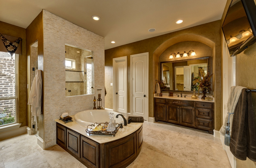 Design ideas for an expansive mediterranean master bathroom in Dallas with an undermount sink, recessed-panel cabinets, dark wood cabinets, marble benchtops, a double shower, a one-piece toilet, beige tile, stone tile, brown walls, travertine floors and a drop-in tub.