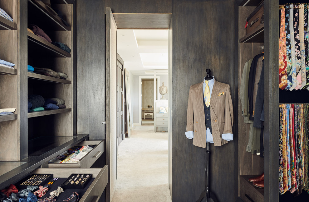 Photo of a medium sized contemporary walk-in wardrobe for men in London with dark wood cabinets and carpet.