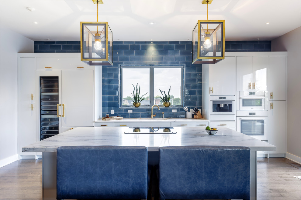 Contemporary single-wall eat-in kitchen in Indianapolis with flat-panel cabinets, white cabinets, blue splashback, subway tile splashback, white appliances, light hardwood floors and with island.