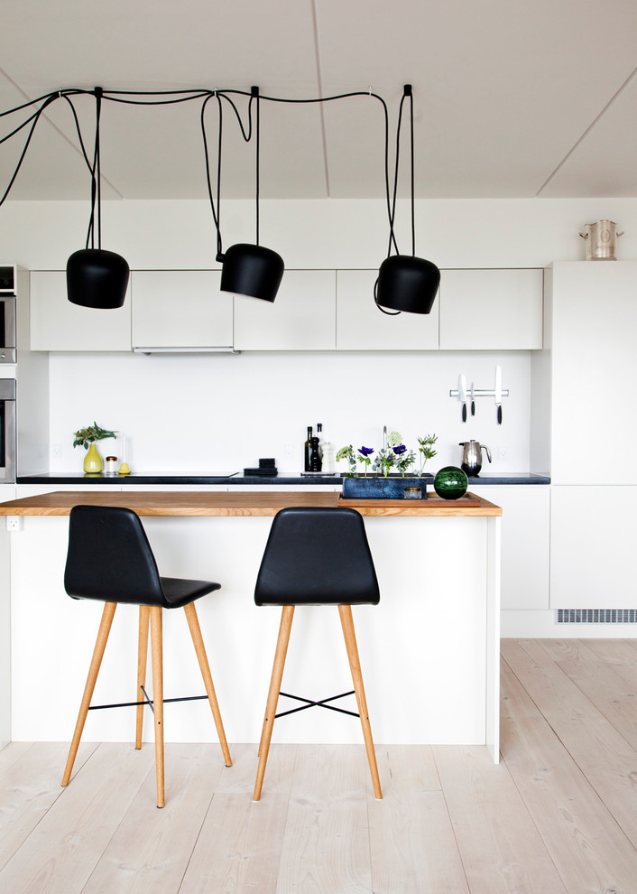 Inspiration for a mid-sized scandinavian galley eat-in kitchen in Copenhagen with flat-panel cabinets, wood benchtops, white splashback, stainless steel appliances, light hardwood floors and with island.