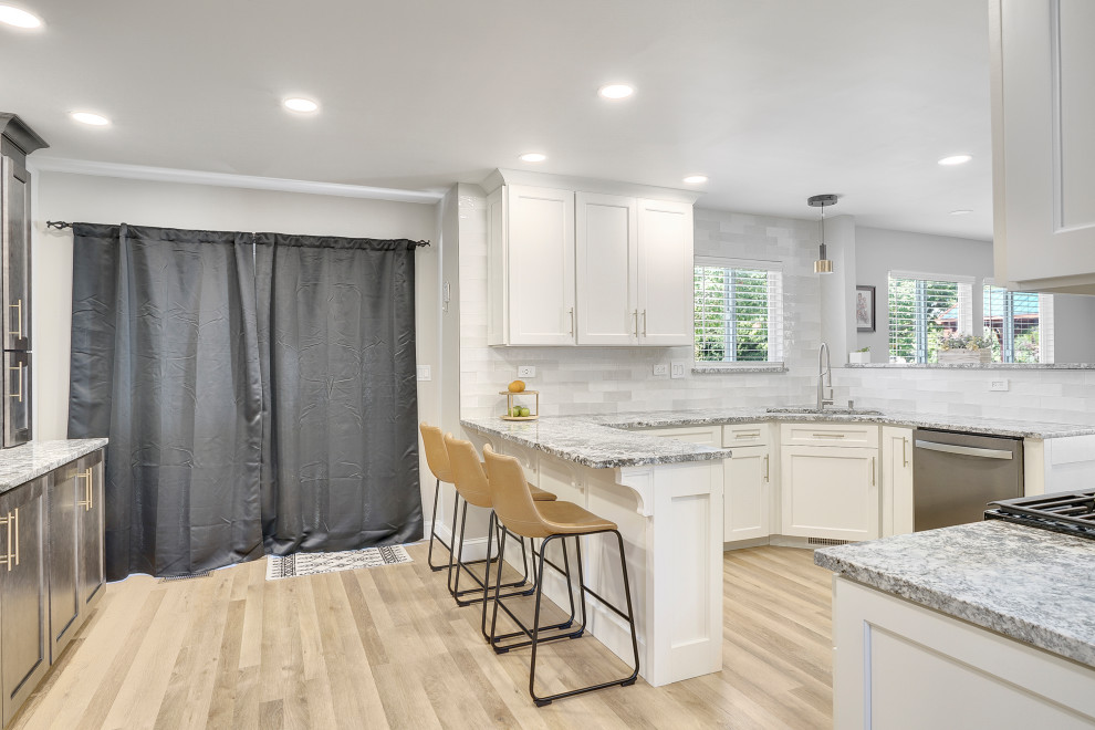 Photo of a mid-sized transitional u-shaped open plan kitchen in Chicago with a single-bowl sink, beaded inset cabinets, white cabinets, marble benchtops, white splashback, ceramic splashback, stainless steel appliances, vinyl floors, a peninsula, beige floor and grey benchtop.