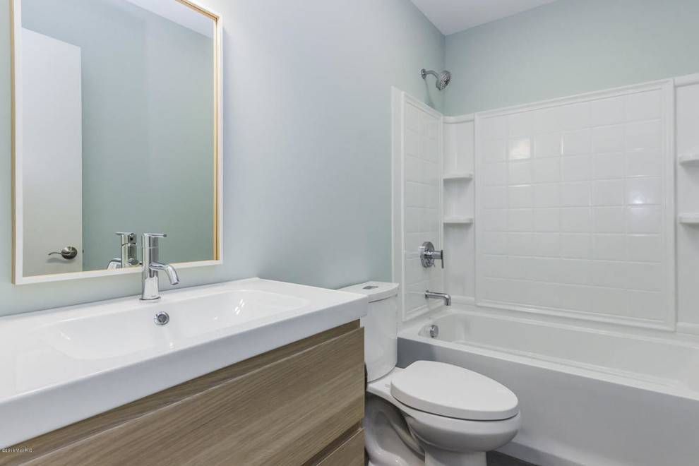 Inspiration for a mid-sized transitional kids bathroom in Grand Rapids with an integrated sink, flat-panel cabinets, light wood cabinets, an alcove tub, a shower/bathtub combo, a two-piece toilet, white tile, blue walls, vinyl floors and solid surface benchtops.