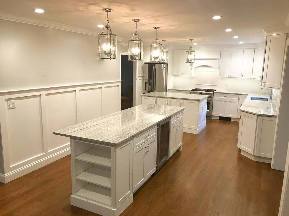 Example of a large transitional l-shaped dark wood floor and brown floor enclosed kitchen design with an undermount sink, shaker cabinets, white cabinets, marble countertops, white backsplash, ceramic backsplash, stainless steel appliances and two islands