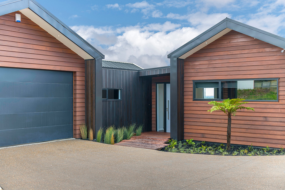 This is an example of a large contemporary one-storey brown house exterior in Auckland with wood siding, a gable roof and a metal roof.