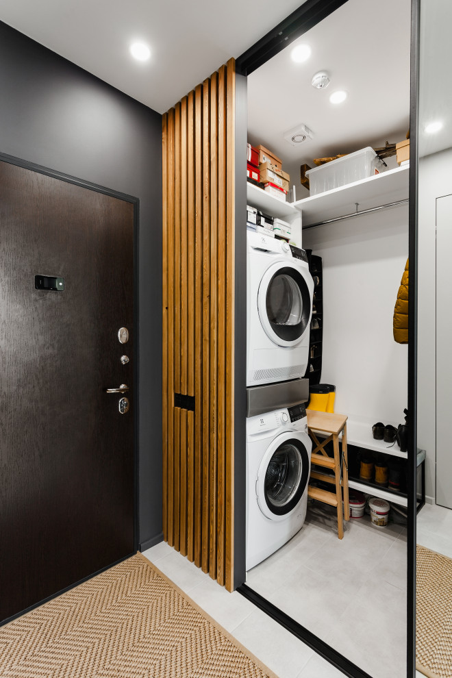 Mid-sized contemporary single-wall laundry cupboard in Moscow with light wood cabinets, white walls, porcelain floors, a stacked washer and dryer, white floor and wood walls.