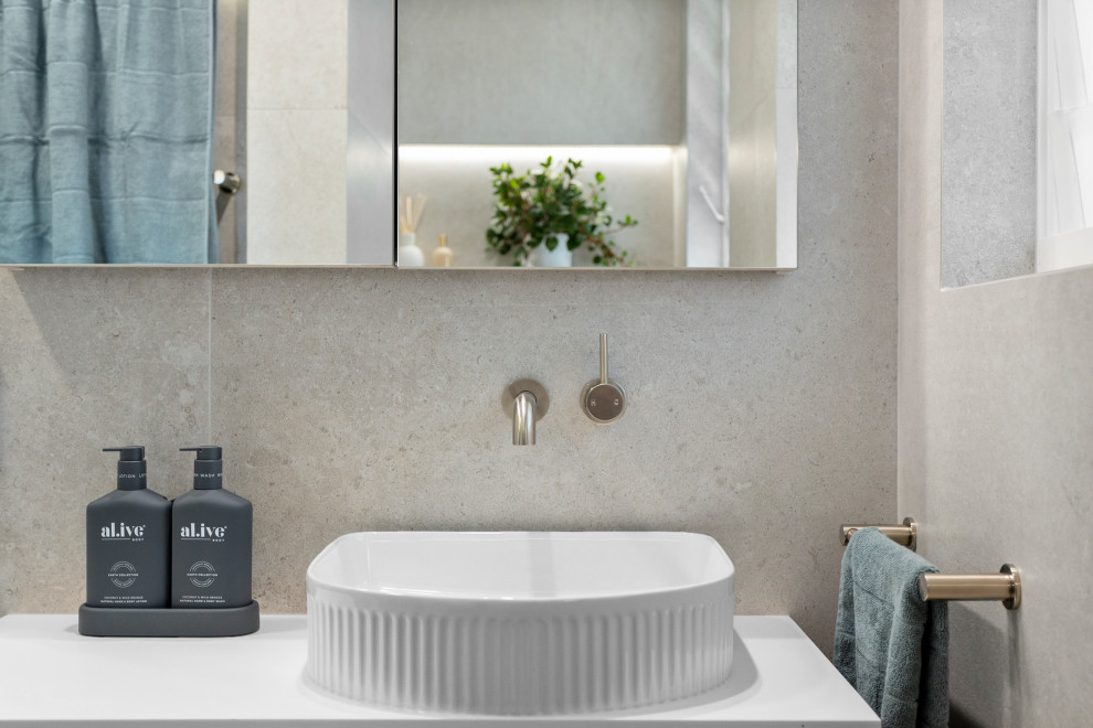 Inspiration pour une petite salle de bain design en bois clair avec un placard en trompe-l'oeil, WC à poser, un carrelage gris, des carreaux de céramique, un mur gris, un sol en carrelage de céramique, une vasque, un plan de toilette en surface solide, un sol gris, une cabine de douche à porte battante, un plan de toilette blanc, une niche, meuble simple vasque et meuble-lavabo suspendu.