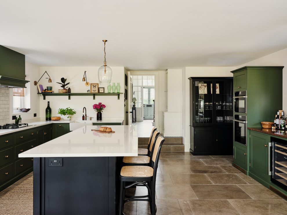 Design ideas for a large transitional l-shaped eat-in kitchen in Other with a farmhouse sink, shaker cabinets, green cabinets, solid surface benchtops, black appliances, limestone floors, with island and grey floor.