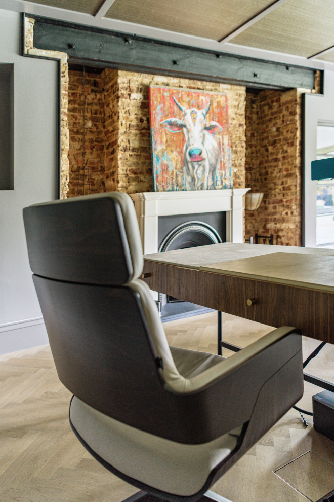 Mid-sized contemporary study room in London with grey walls, a standard fireplace, a brick fireplace surround, a freestanding desk, grey floor and brick walls.
