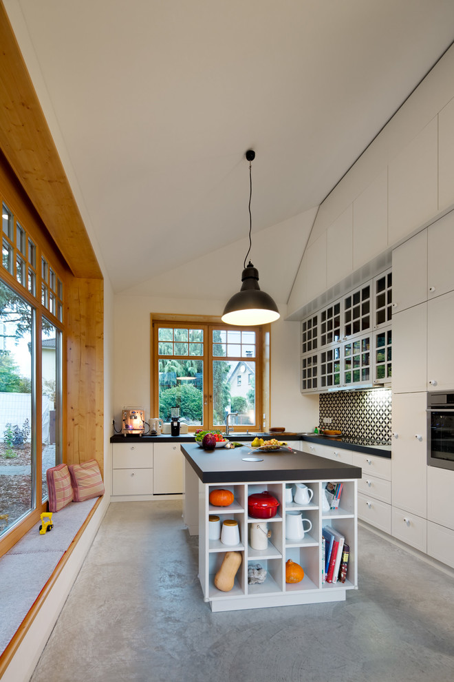 Photo of a large contemporary l-shaped separate kitchen in Leipzig with glass-front cabinets, multi-coloured splashback, concrete floors, with island, panelled appliances and ceramic splashback.