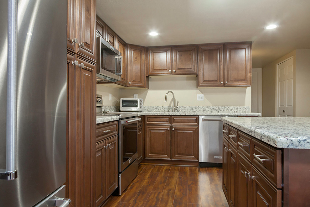 Example of a mid-sized transitional l-shaped laminate floor and brown floor enclosed kitchen design in Phoenix with an undermount sink, shaker cabinets, medium tone wood cabinets, granite countertops, multicolored backsplash, stone slab backsplash, stainless steel appliances and an island