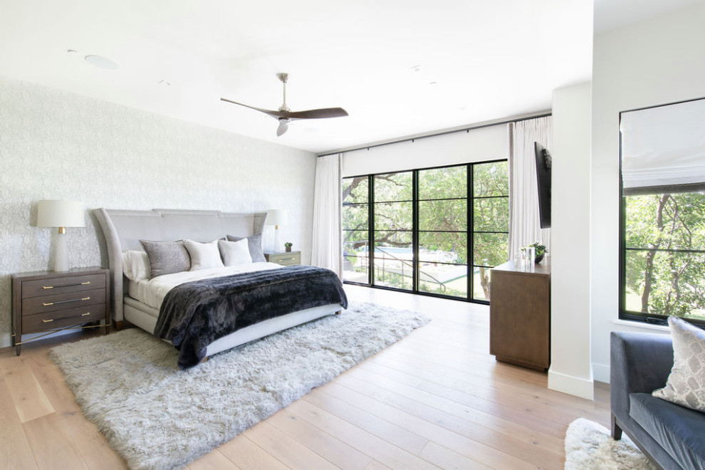 Large transitional master bedroom in Austin with white walls, light hardwood floors, a standard fireplace, a metal fireplace surround and wallpaper.