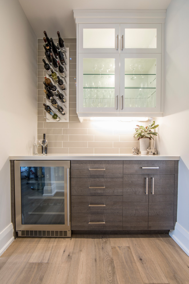 Large contemporary l-shaped open plan kitchen in Toronto with an undermount sink, shaker cabinets, white cabinets, solid surface benchtops, grey splashback, subway tile splashback, stainless steel appliances, light hardwood floors, with island, beige floor and white benchtop.