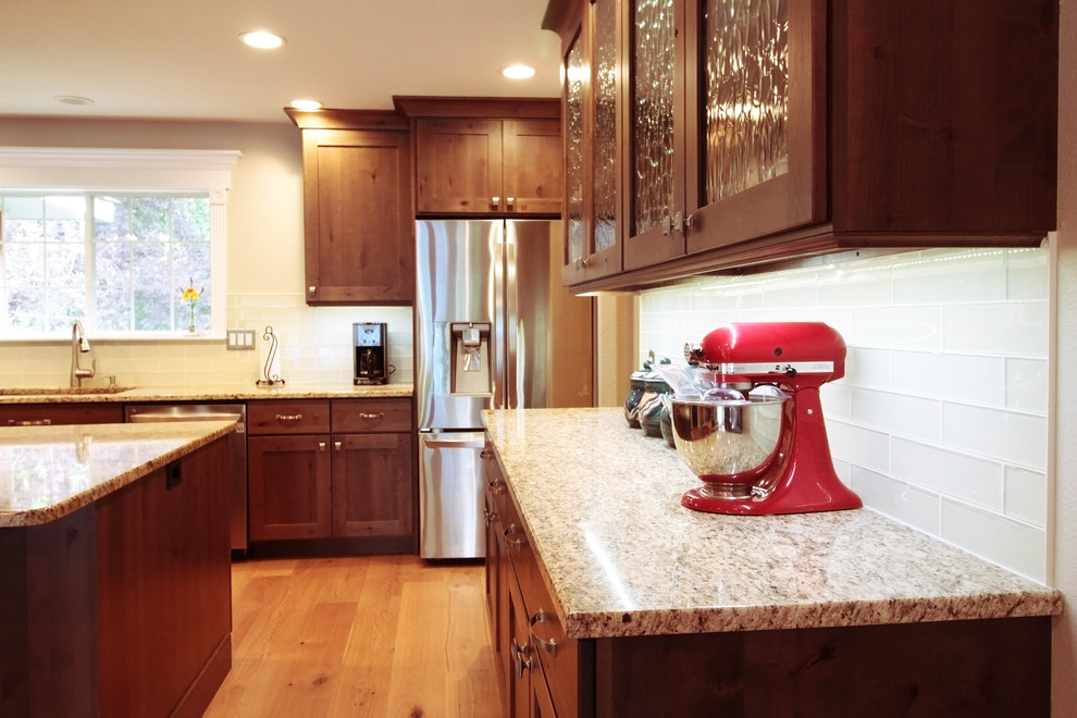 Example of a large mountain style u-shaped light wood floor and brown floor open concept kitchen design in Boise with an undermount sink, shaker cabinets, brown cabinets, granite countertops, white backsplash, glass tile backsplash, stainless steel appliances and an island