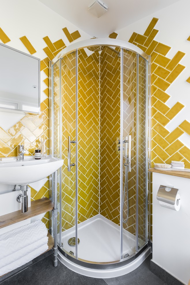 Photo of a small contemporary master bathroom in London with open cabinets, light wood cabinets, a corner shower, a wall-mount toilet, yellow tile, ceramic tile, white walls, concrete floors and a wall-mount sink.