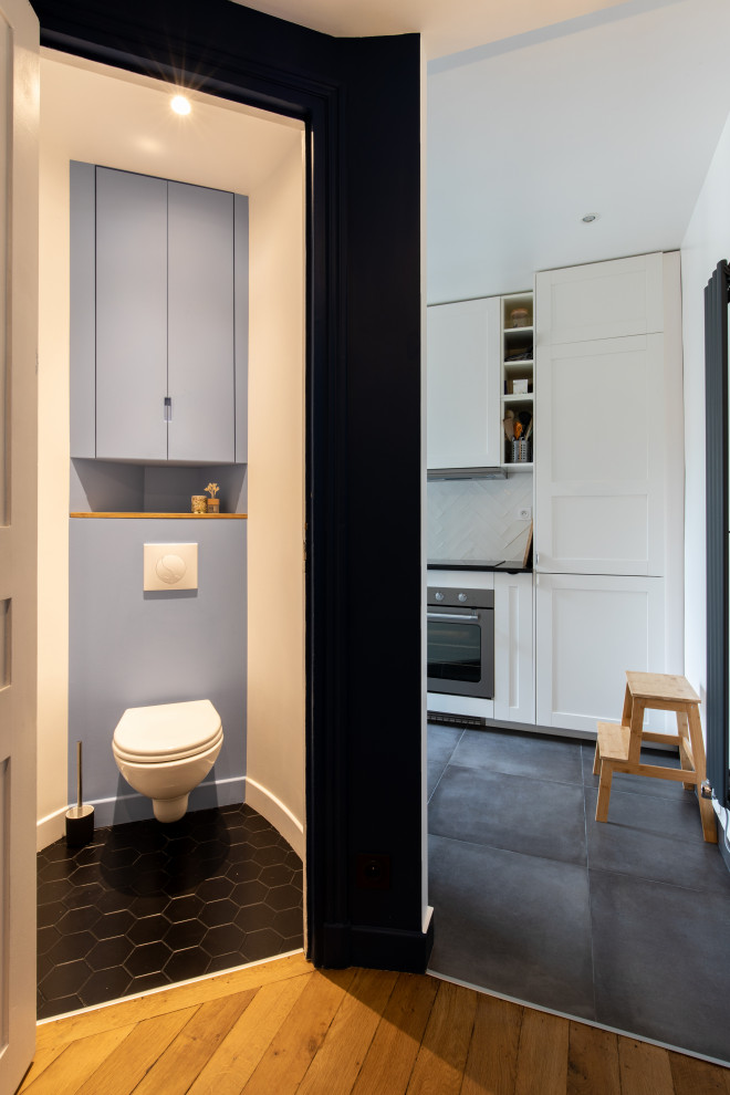 Small contemporary powder room in Paris with beaded inset cabinets, blue cabinets, a wall-mount toilet, ceramic floors, black floor and a built-in vanity.