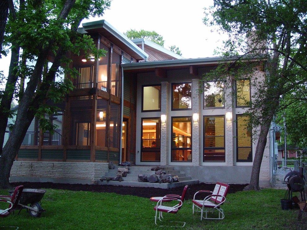 This is an example of a mid-sized modern two-storey beige house exterior in Austin with stone veneer and a flat roof.