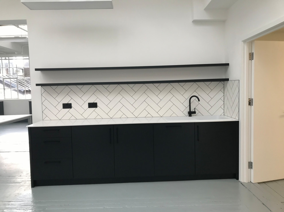 Example of a small trendy single-wall laminate floor and gray floor enclosed kitchen design in London with a single-bowl sink, flat-panel cabinets, black cabinets, solid surface countertops, white backsplash, ceramic backsplash, paneled appliances, no island and white countertops