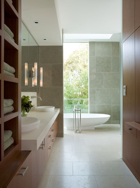 Свежая идея для дизайна: большая главная ванная комната в стиле модернизм с плоскими фасадами, фасадами цвета дерева среднего тона, отдельно стоящей ванной, душем без бортиков, унитазом-моноблоком, плиткой из известняка, белыми стенами, полом из известняка, настольной раковиной, столешницей из известняка, бежевым полом, душем с распашными дверями, белой столешницей, тумбой под две раковины и встроенной тумбой - отличное фото интерьера