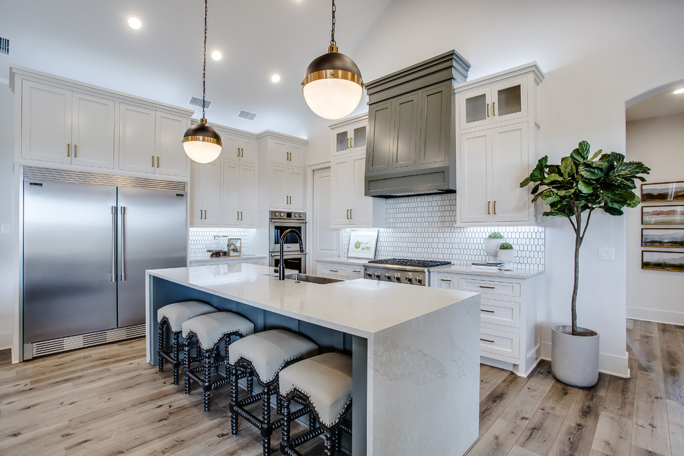 Inspiration for a mid-sized transitional l-shaped medium tone wood floor and brown floor open concept kitchen remodel in Austin with a farmhouse sink, shaker cabinets, white cabinets, marble countertops, white backsplash, stainless steel appliances, an island and white countertops