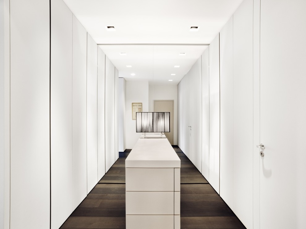 This is an example of a large modern gender-neutral dressing room in Frankfurt with flat-panel cabinets, white cabinets and dark hardwood floors.