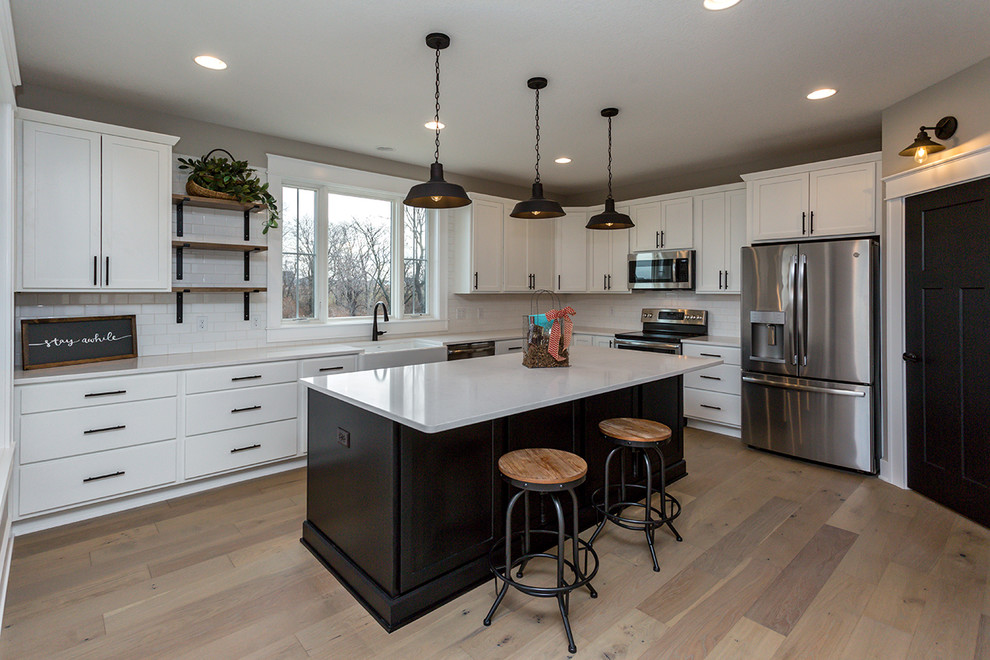 Inspiration for a l-shaped light wood floor and beige floor enclosed kitchen remodel with a farmhouse sink, shaker cabinets, white cabinets, white backsplash, stainless steel appliances, an island and white countertops