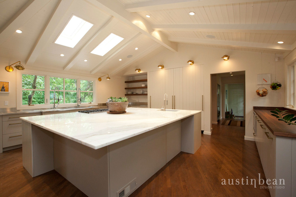 Inspiration for a large transitional u-shaped medium tone wood floor eat-in kitchen remodel with an integrated sink, flat-panel cabinets, white cabinets, stainless steel countertops, white backsplash, stone slab backsplash, stainless steel appliances and white walls