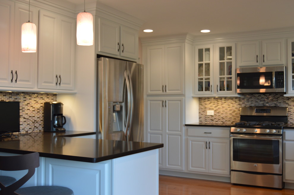 Inspiration for a mid-sized transitional l-shaped medium tone wood floor eat-in kitchen remodel in Chicago with quartzite countertops, an island, a single-bowl sink, raised-panel cabinets, white cabinets, multicolored backsplash, glass tile backsplash and stainless steel appliances